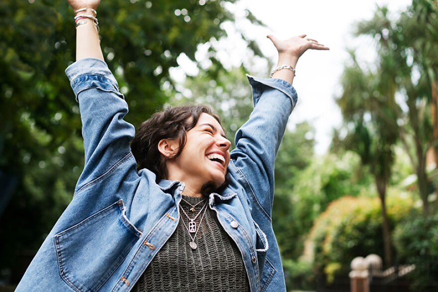 Happy woman outdoors with arms raised as mood booster