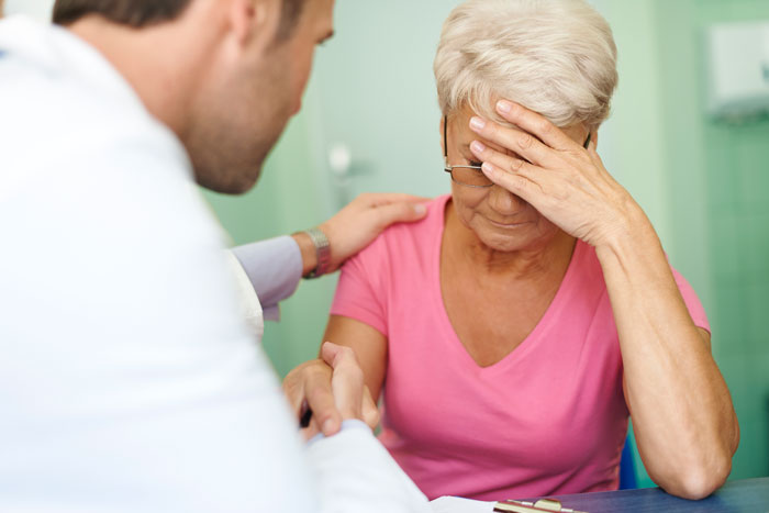 Doctor comforting elderly woman with headache in medical setting