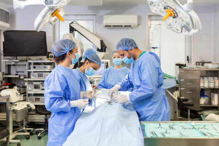 A team of medical professionals performing surgery, dressed in blue scrubs, masks, and hairnets. This represents people crossing to the other side in a medical context.