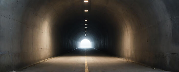 A long, dark concrete tunnel with a bright light at the end, symbolizing stories from the other side.