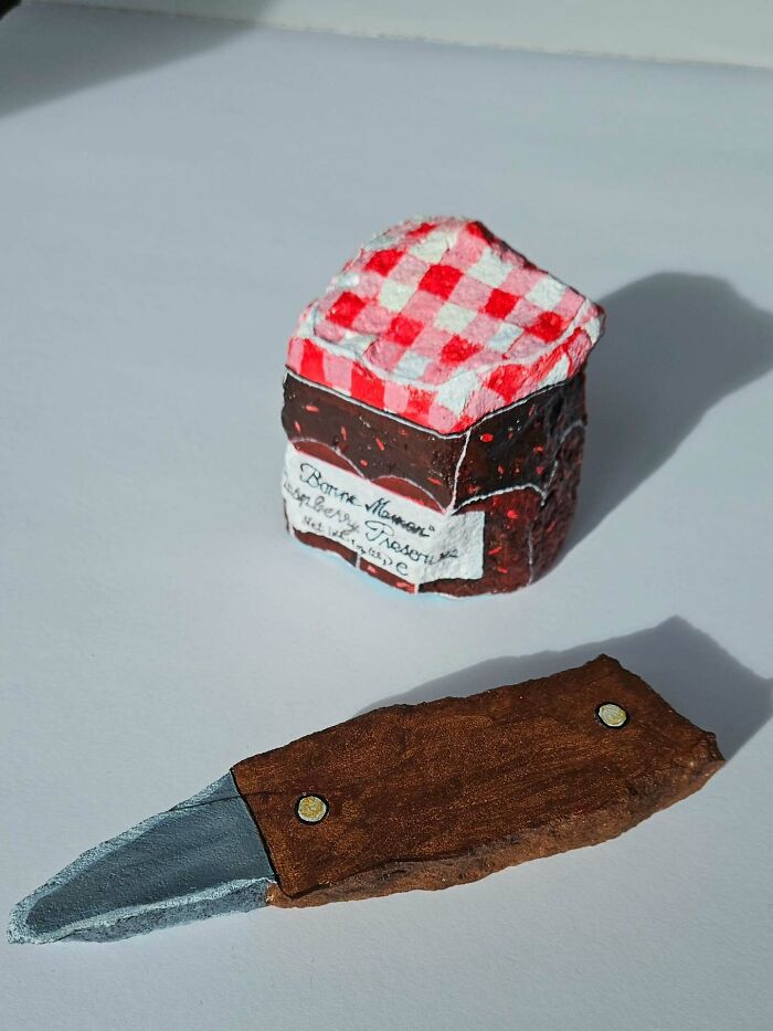 A colorful stone creation resembling a jar of raspberry jam with a red checkered top and a small knife.