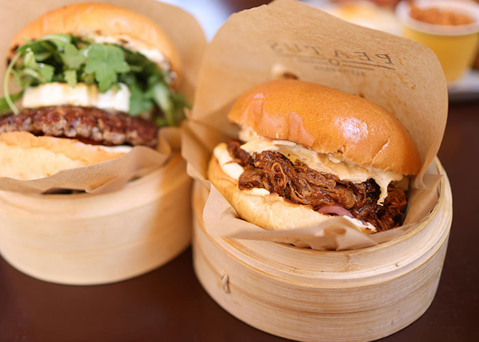 Two gourmet burgers, one with pulled pork and another with a patty and arugula, served in bamboo steamers. Debunking US stereotypes.