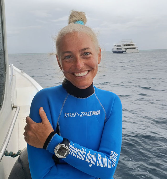 Smiling diver woman in blue wetsuit on boat in Maldives diving scene
