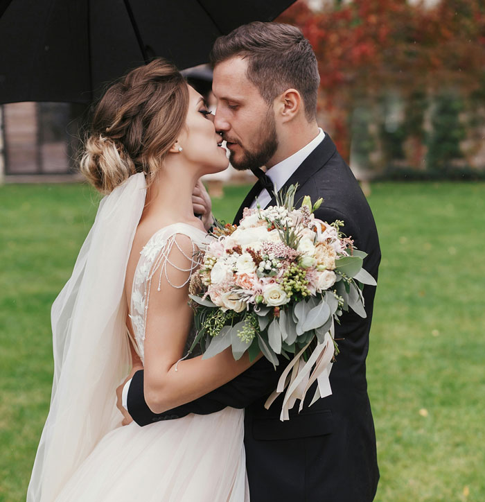 Bride and groom embracing outdoors with wedding bouquet