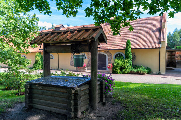 Rustic garden well with bucket and house in sunny backyard