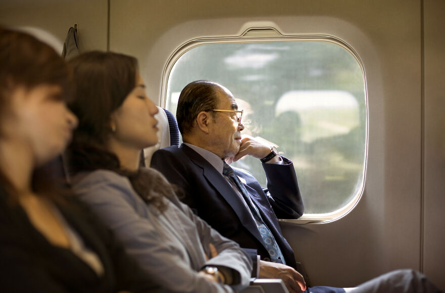Passengers on a Japanese bullet train, an older man in a suit looking out the window, showing amazing Japanese things.