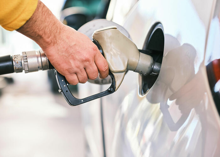 A person's hand refilling a car with gas, illustrating worries about the economy and wallets due to rising fuel costs.