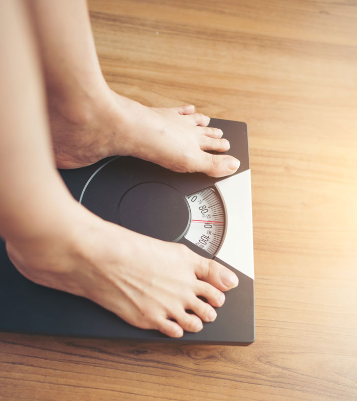 Bare feet on a bathroom scale on a wooden floor, with sunlight. Debunking wrong facts about weight and health on Reddit.