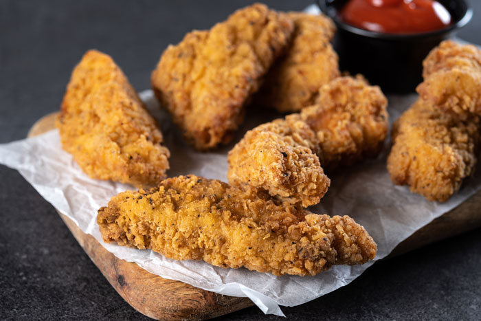 Crispy artisinal fried chicken pieces on wooden board with sauce