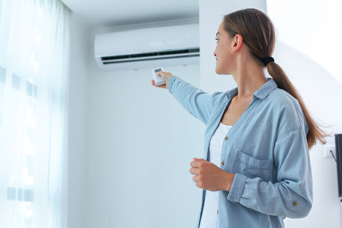 Woman using remote to control air conditioning system indoors in Europe