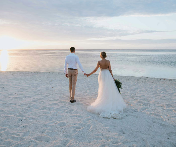 Bride and groom holding hands walking on beach at sunset wedding photography