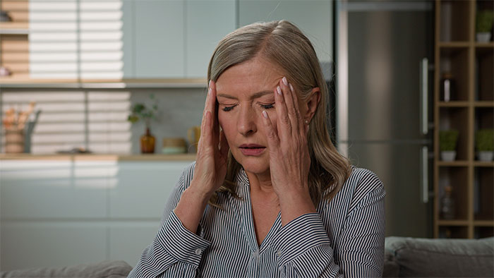 A distressed woman holding her temples, eyes closed, reflecting the intense MIL grandchild drama.