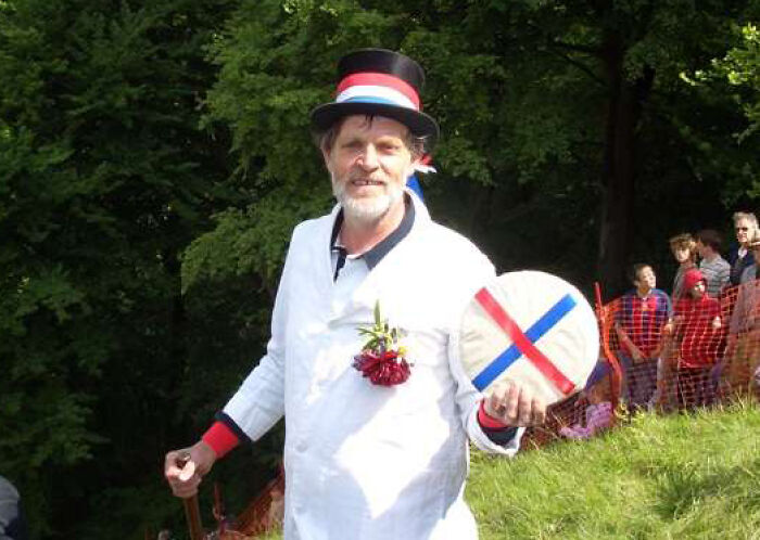 Man dressed in traditional attire with a top hat and decorated drum outdoors
