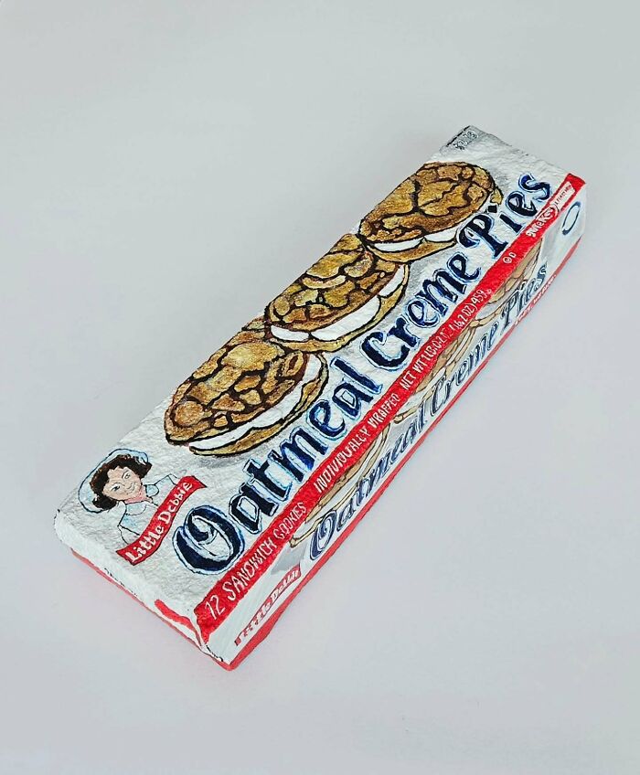 A colorful stone creation painted to look like a box of Little Debbie Oatmeal Creme Pies, showcasing iconic foods.