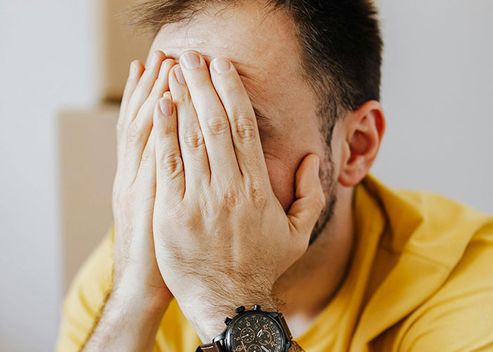 A man in a yellow shirt covers his face with his hands, displaying frustration, possibly related to things people of low intelligence do.