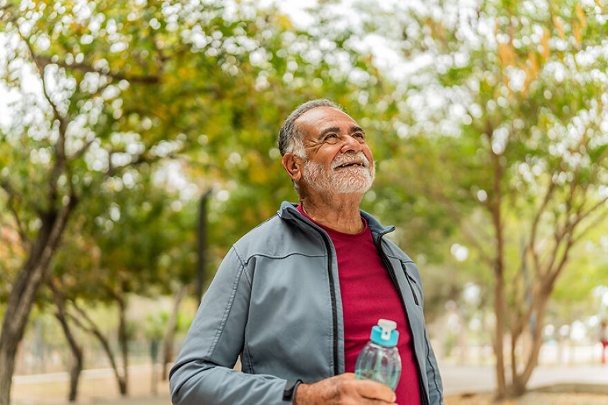 Senior man holding water bottle smiling during outdoor mood boost walk