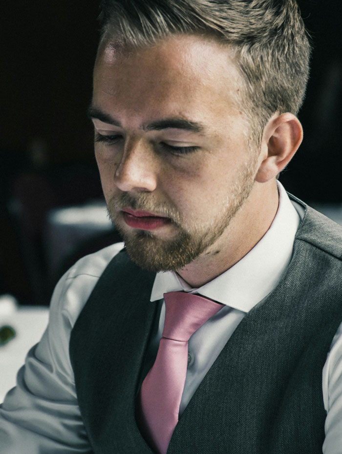 Groom wearing pink tie looking down contemplative wedding photography