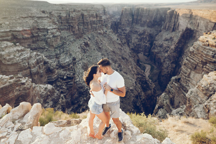 A couple embracing atop a cliff overlooking a canyon, sharing a tender moment. A romantic engagement story scene.