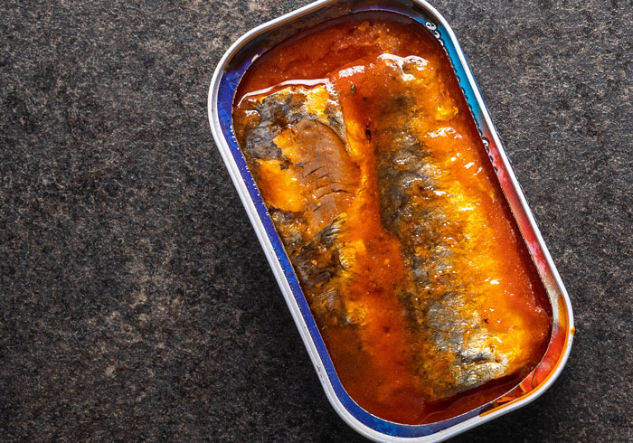 Overhead shot of an open can of sardines in a rich tomato sauce, one of the weirdest packages mailmen had to deliver.
