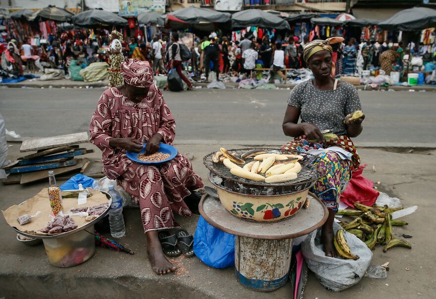 Two women on a street, one shelling peanuts, the other preparing plantains for grilling. Reflects challenges in countries with the worst diets.