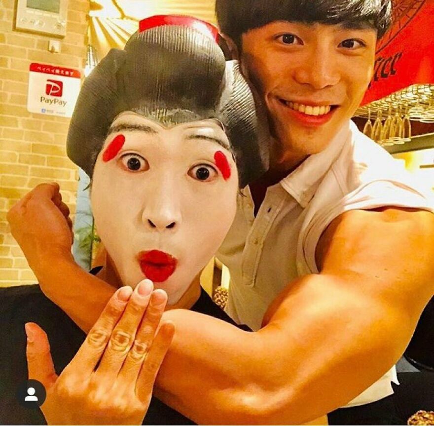 A smiling man showing his bicep next to someone in geisha-like makeup. Highlighting unique Japanese things.