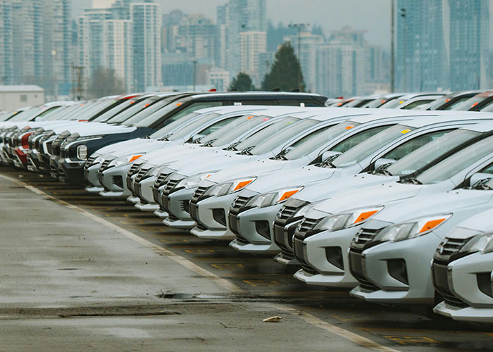Row of new cars, signifying supply chain issues and economic impact, making people worry about the economy and their wallets.
