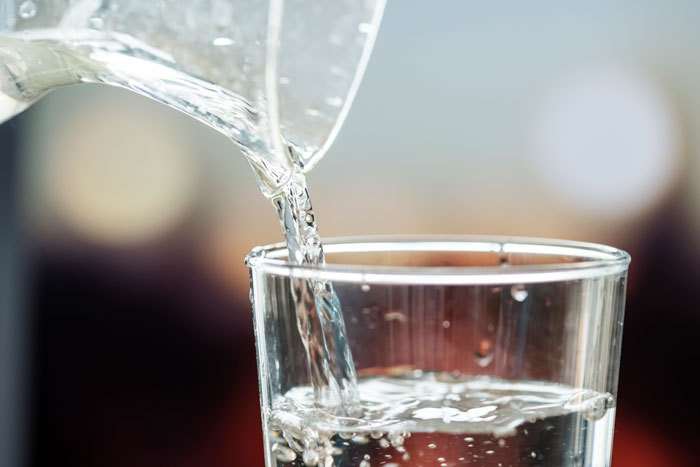 Clear water pouring from a glass pitcher into a drinking glass, illustrating a very wrong fact or common misconception.