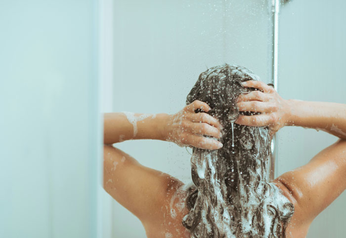 A person washing their hair with shampoo and lather in a shower. A luxury poor people often dream of.