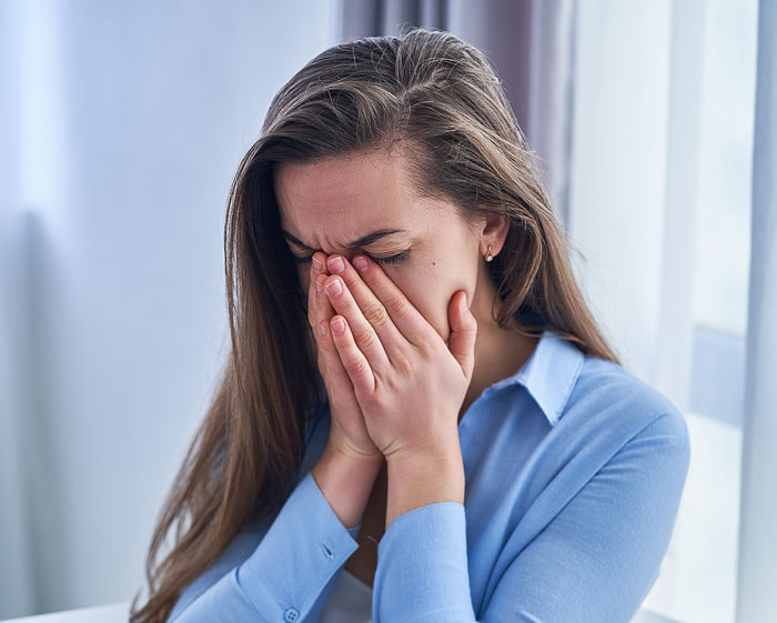 Woman upset and crying with hands covering her face indoors