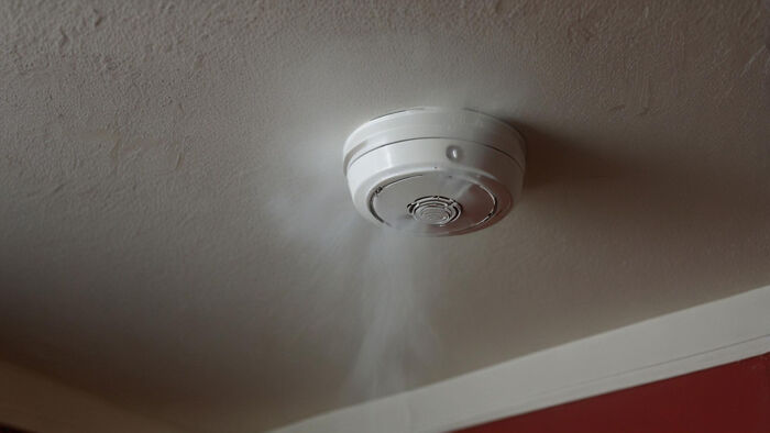 A white smoke detector on a ceiling emitting smoke. Savage things can happen, requiring safety measures like these.