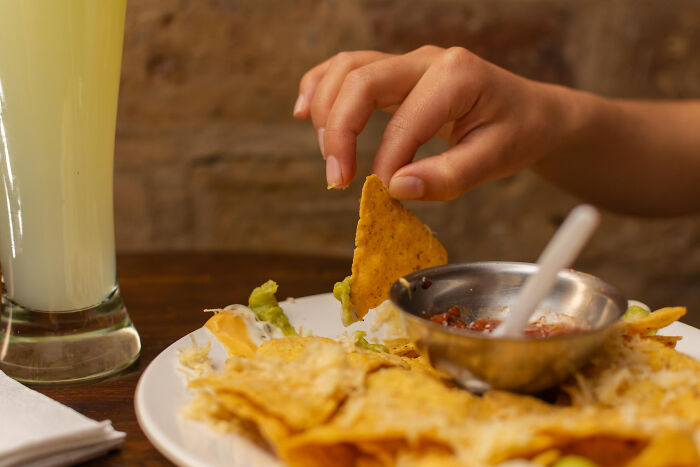Hand grabbing chip from nachos with dip on table