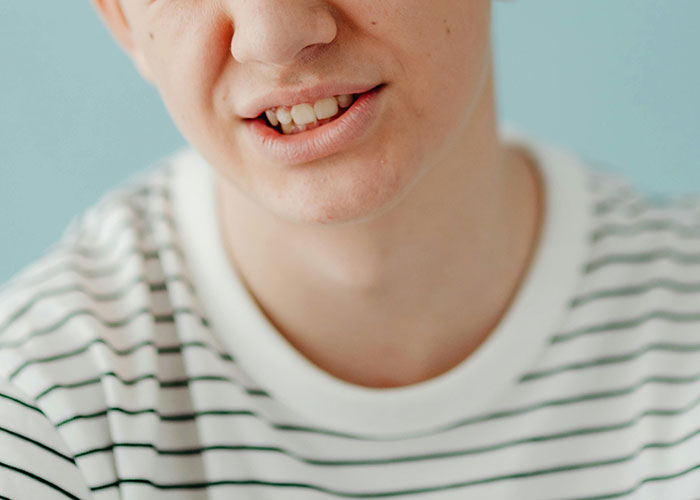 Close-up of a person's mouth with a slight smile, showing teeth, wearing a striped shirt. Debunking US stereotypes.