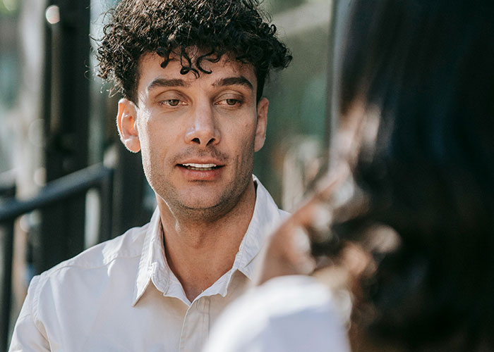 A man with curly hair and a light shirt talking, focusing on behaviors that indicate low intelligence.