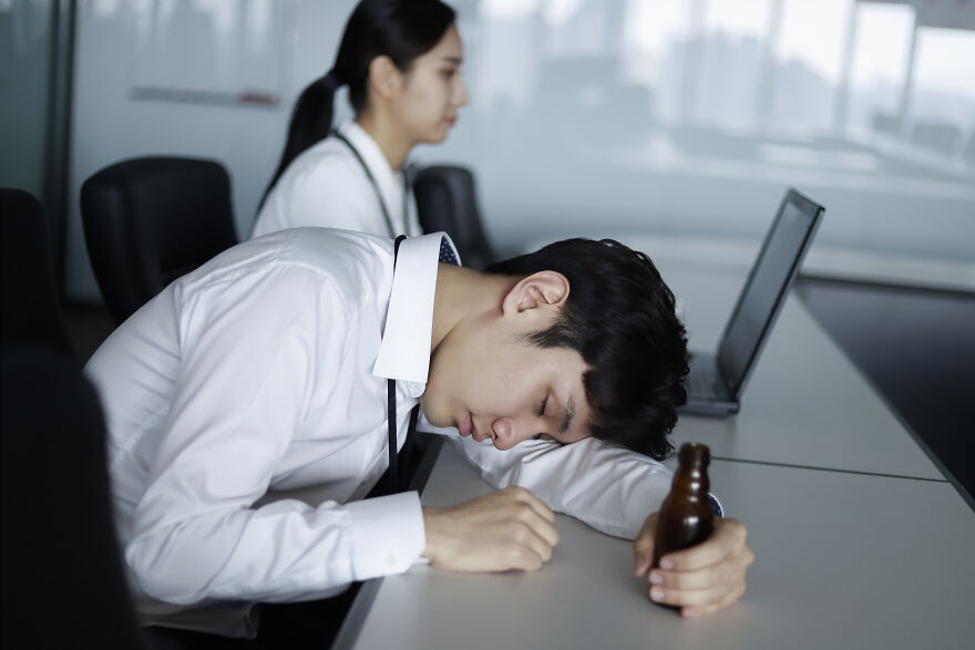 A Japanese man asleep at his desk, holding a beer bottle. Many countries should have better work-life balance.