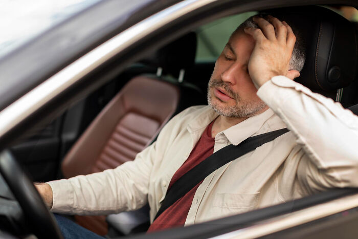 Tired man resting head on hand inside car wearing seatbelt