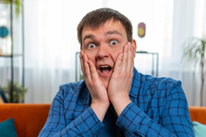 A man in a blue plaid shirt looks shocked, hands on his cheeks, embodying hilarious engagement stories and chaos.