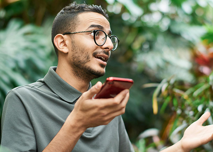 A man with glasses speaks into a red phone, hand gesturing. His animated expression suggests deep thought about intelligence.