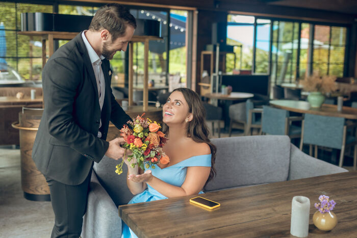A man giving flowers to a happy woman at a restaurant. Engagement stories and romance.