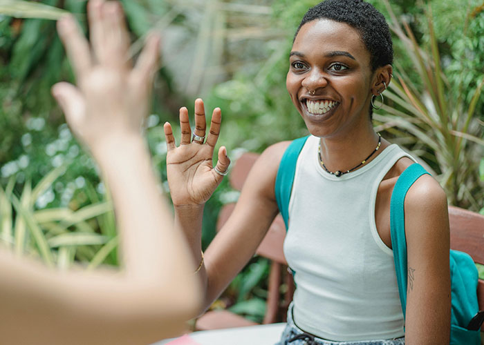 A young woman with short curly hair and a nose ring smiles, high-fiving someone. Debunk US stereotypes.
