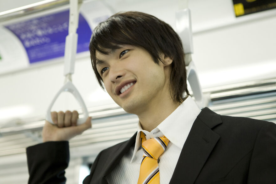 A smiling young man in a suit and tie holding a Japanese train handle. Experience these amazing Japanese things.