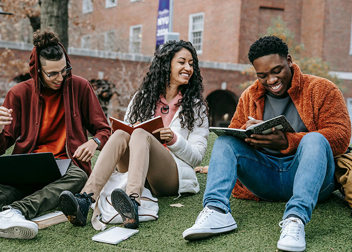 Three diverse students smiling and studying outdoors. Debunking stereotypes about the US in education.