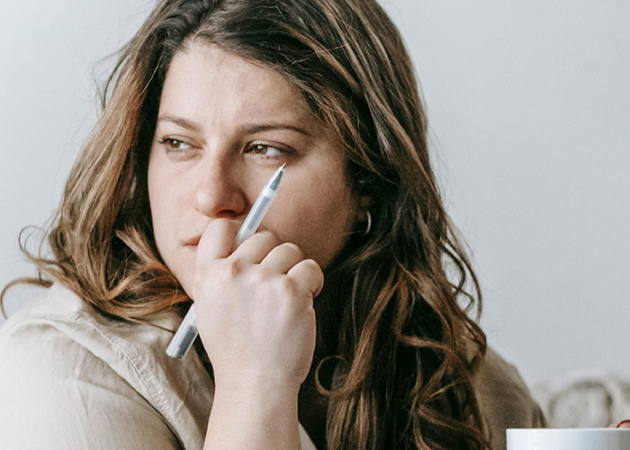 A pensive woman with long hair holds a pen to her face, reflecting on common things people of low intelligence do.