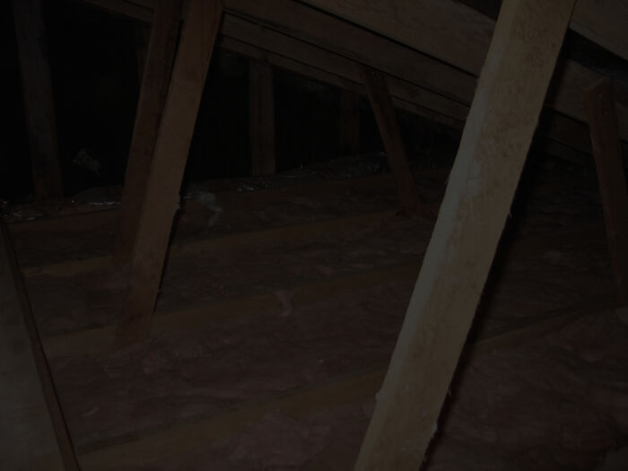 Dark attic space with wooden beams and insulation visible