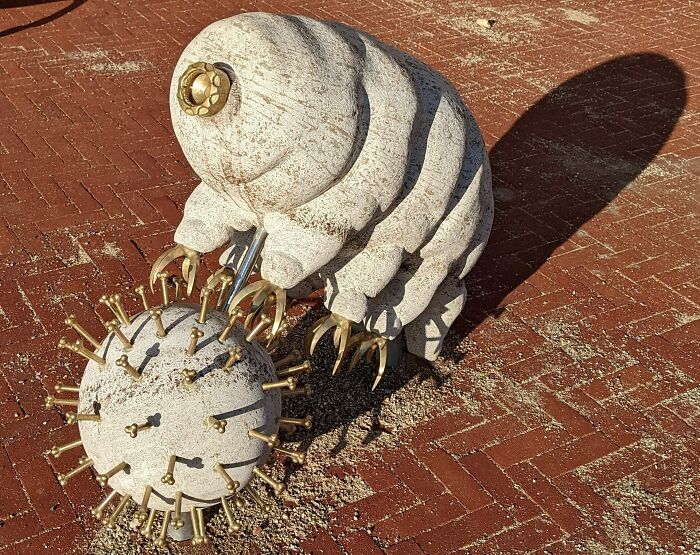 Sculpture of a tardigrade battling a virus on brick pavement, showcasing scientific facts about everything.