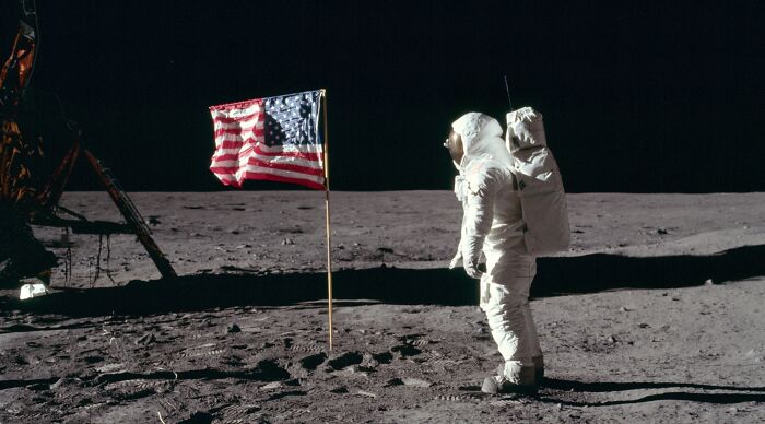 Astronaut on the moon next to American flag during historic space mission Astronaut on the moon next to American flag during historic space mission