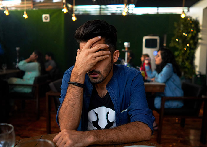 Man in cafe stressed and covering his face reflecting relationship strain