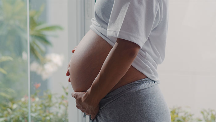 Pregnant person holding belly near window showing early marriage challenges