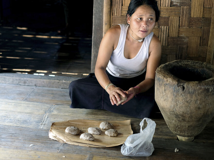 A woman in a white tank top and dark skirt shapes food balls, possibly indicating diets in certain countries.
