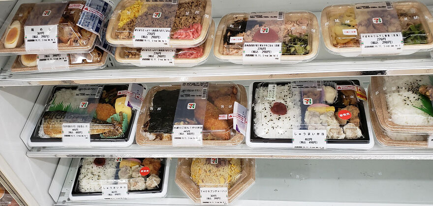 A refrigerated display case filled with various Japanese bento boxes and ready-to-eat meals at a 7-Eleven store.