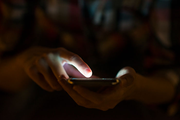 Person using smartphone with glowing screen in dim light